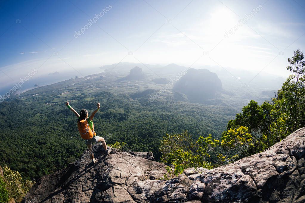 cheering young woman with backpack standing on mountain top 
