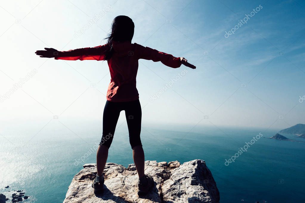 young woman standing with outstretched arms on sunrise windy coast