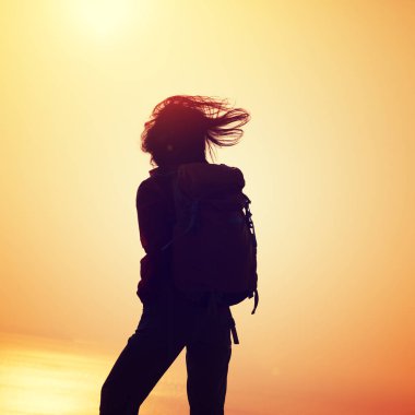 Sırt çantası ayakta gündoğumu rüzgarlı kenarı olan kadın