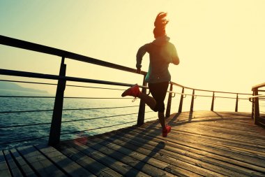 Güneş doğarken sahil kenarında koşan sportif fitness kadın koşucusu