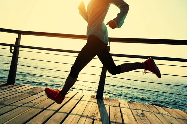 日出时跑在海滨木板路上的体态健壮的女跑步者 — 图库照片
