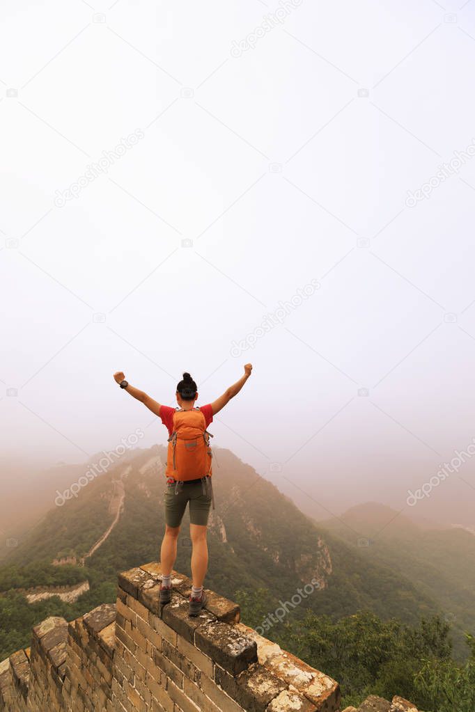 successful female hiker standing with open arms to the great wall on the top of mountain