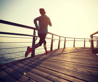 Güneş doğarken sahil kenarında koşan sportif fitness kadın koşucusu