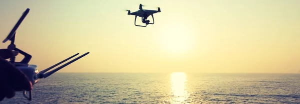 woman holding remote control of flying drone which taking photo over sunrise sea