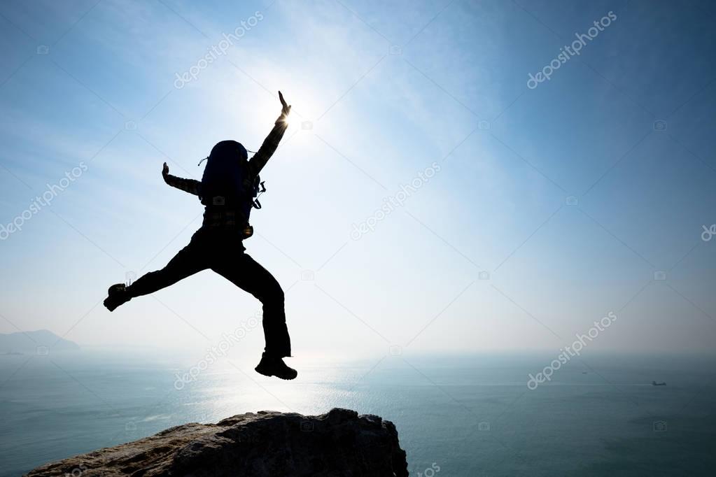 female hiker jumping on sunrise seaside cliff edge