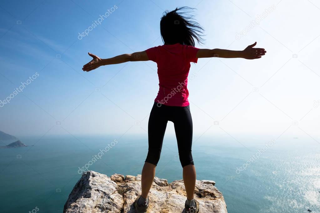 Woman standing with outstretched arms on sunrise windy coast
