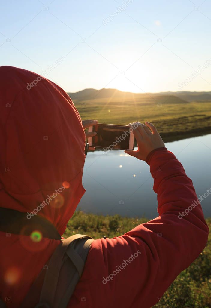 Tourist taking photo with smartphone in beautiful sunset landscape