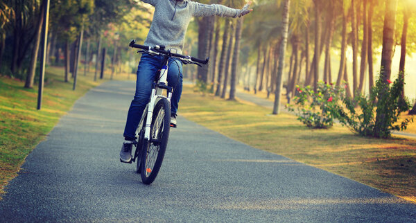 woman cyclist riding bike with outstretched arms in tropical park