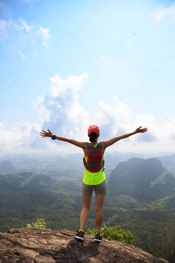 successful female with outstretched arms to the beautiful landscape on mountain top