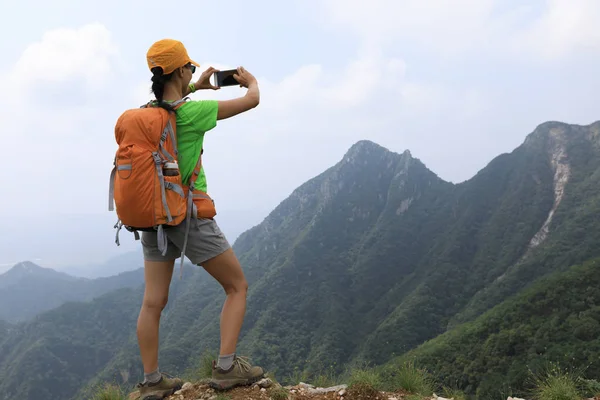 山の上にスマート フォンで写真を撮る女性バックパッカー — ストック写真
