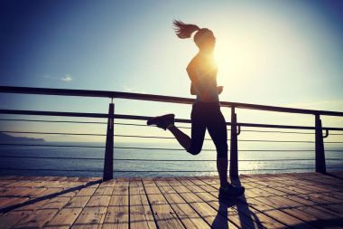 Güneş doğarken sahil kenarında koşan sportif fitness kadın koşucusu 