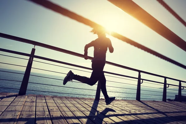 在日出时在海滨木板上奔跑的运动型女性赛跑者 — 图库照片