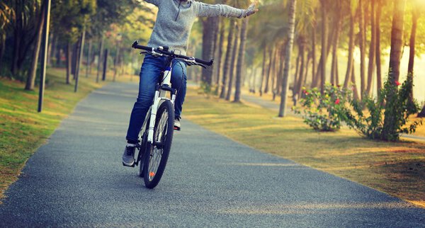 женщина-велосипедистка на велосипеде с вытянутыми руками в тропическом парке
