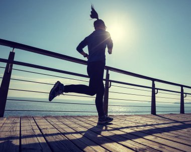 Sahil sahil üzerinde gündoğumu sırasında çalışan sportif genç kadın 