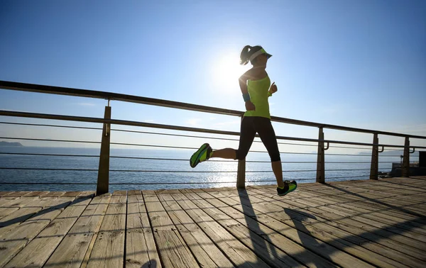 在日出时在海滨木板上奔跑的运动健身妇女 — 图库照片