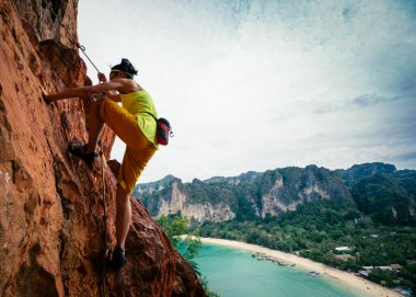 woman rock climber climbing on seaside cliff clipart