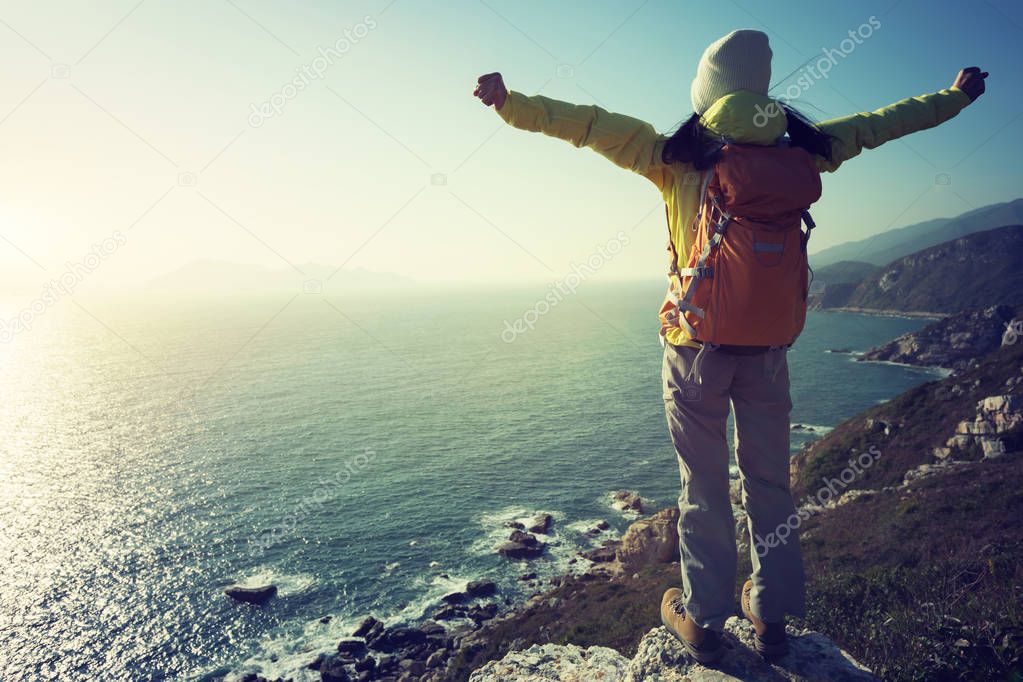 successful female hiker standing on sunrise seaside mountain cliff edge
