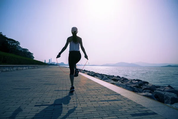 运动的年轻健身女子跳绳在海岸小道上 — 图库照片