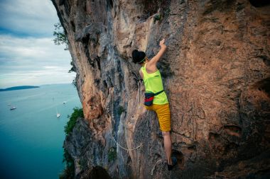 female rock climber climbing on seaside cliff clipart