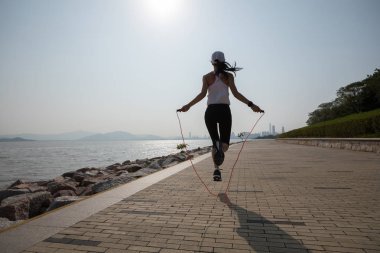 Sportif genç fitness kadın sahil yolu üzerinde ip atlama