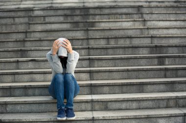 Upset woman sitting alone in city stairs clipart