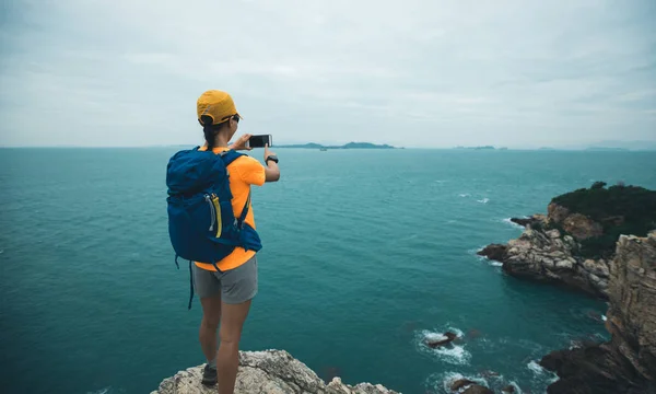 女徒步旅行者在海滨用智能手机拍照 — 图库照片