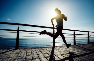 Güneş doğarken sahil kenarında koşan sportif fitness kadın koşucusu
