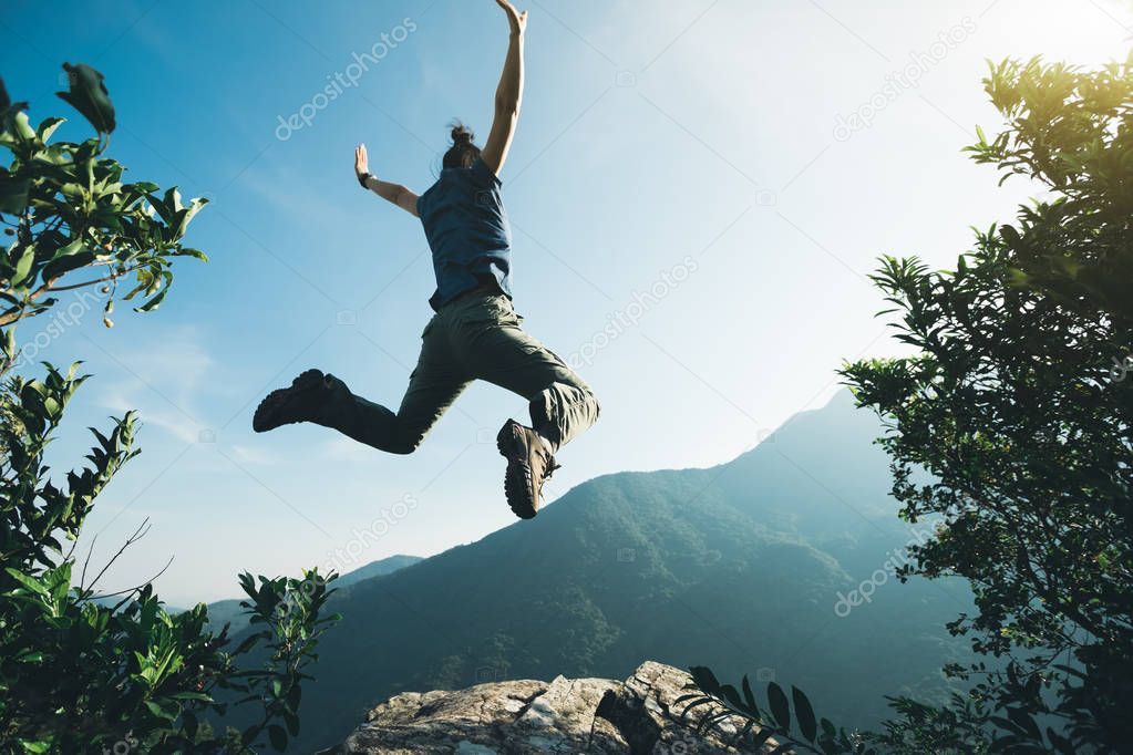 successful hiker jumping on sunrise mountain top