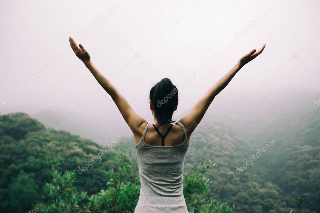 Young woman with outstretched arms enjoying the view on morning mountain valley