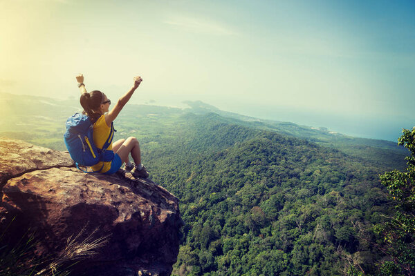 successful woman hiker cheering on mountain peak cliff edge