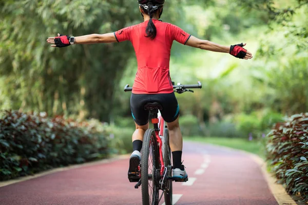 Female cyclist riding mountain bike on tropical rainforest trail with arms outstretched