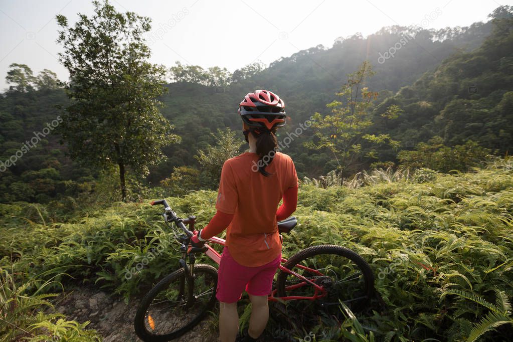 Cross country biking female cyclist with mountain bike on tropical forest trail looking at view