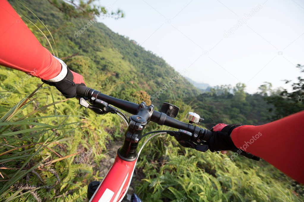 Cross country biking cyclist hands holding handlebar riding mountain bike downhill on tropical forest trail slope