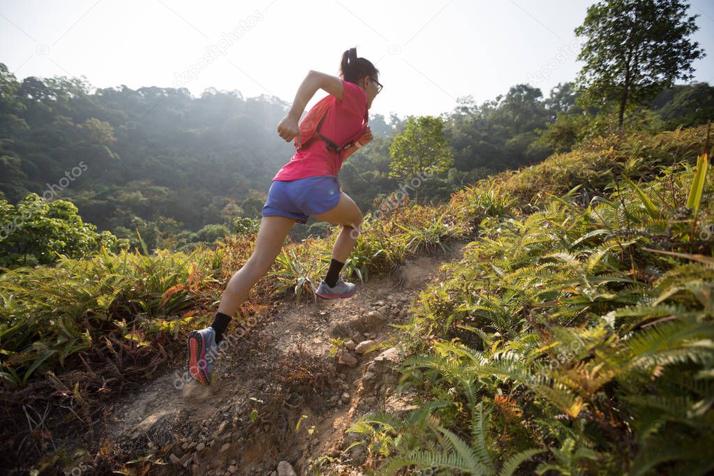 Woman trail running up on mountain slope in tropical forest