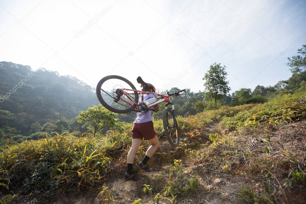 Cross country biking female cyclist with mountain bike climbing up mountain slope on tropical forest trail