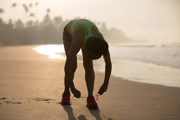 Female runner tying shoelaces ready to run on beach