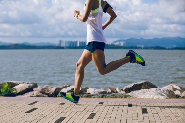 Güneşli sahil yolunda koşan ve maraton koşan spor kadını.