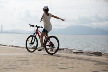 Gündoğumunda deniz kenarında dağ bisikleti süren kadın bisikletçi.