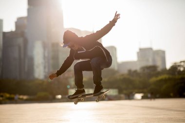 Young skateboarder skateboarding in urban city at sunset clipart