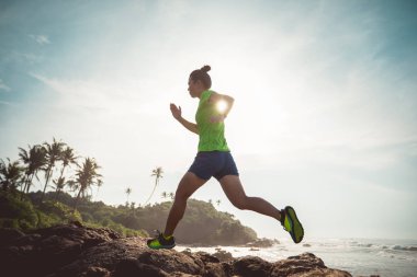 Sahildeki kayalık dağın tepesine koşan dişi ultra maraton koşucusu.