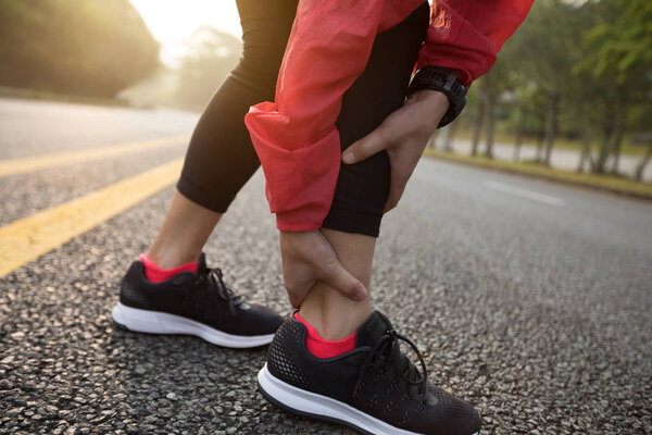 Low section of female runner touching sprained ankle, sport injury