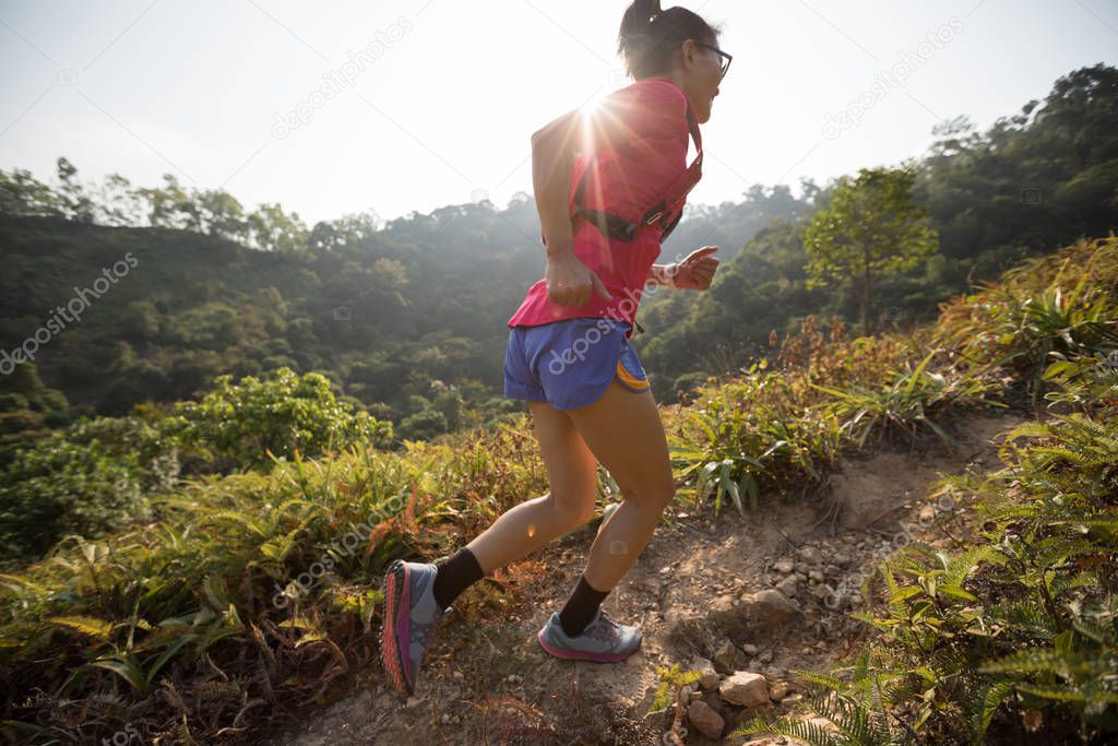 Female trail runner running up on mountain slope in tropical forest