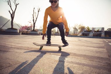 Genç Asyalı kaykaycı güneş ışığında parkta kaykay yapıyor.