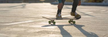 Kadın kaykaycının alçak kısmı gün batımında şehir parkı yolunda kaykaya atlamaya hazır.