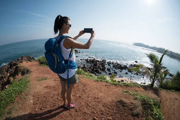 Female hiker in seaside using smartphone and taking picture of sea water