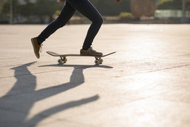Low section of female skateboarder skateboarding at sunset on city road with shadow.