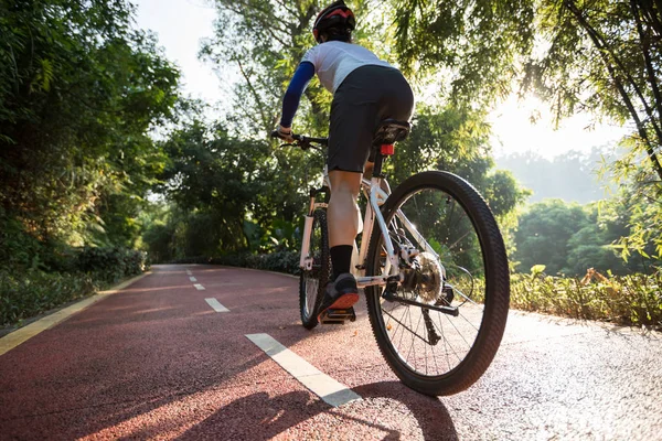日の出の公園の自転車道での女性のサイクリングの背面図 — ストック写真