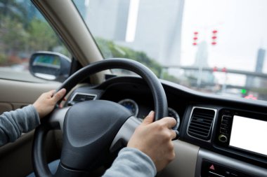 Hands of female driver holding steering wheel while driving car on Asian city road in rainy daytime