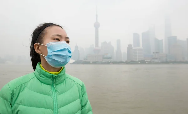 緑のジャケットと顔のマスクで心配アジアの女性は公害霧と街を離れて見て — ストック写真