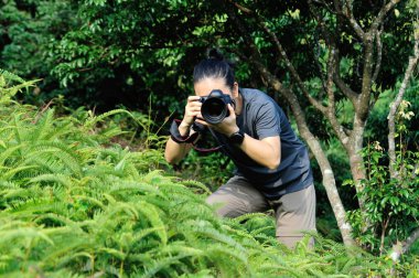 Profesyonel dijital kamerayla yeşil ormanda fotoğraf çeken bir fotoğrafçı.